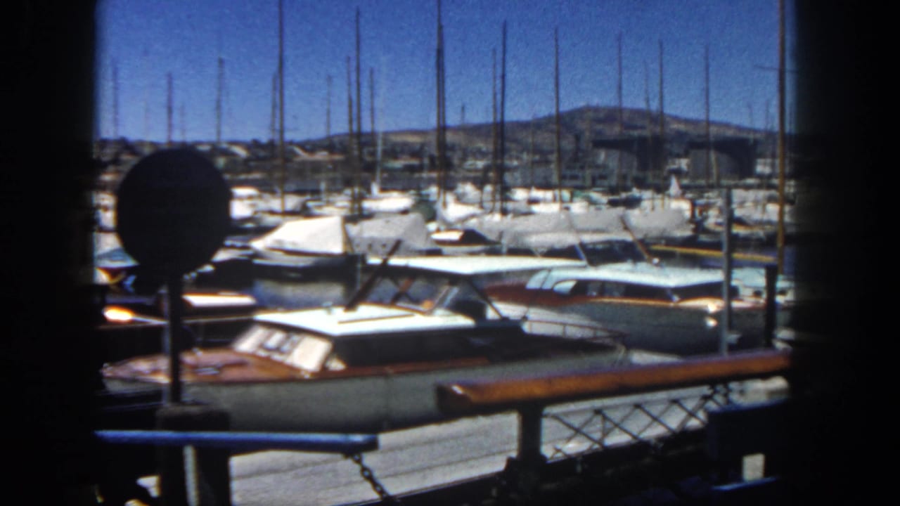 1962 San Diego marina view with cabin boats, sailboat masts, bright sky, and dark foreground framing.