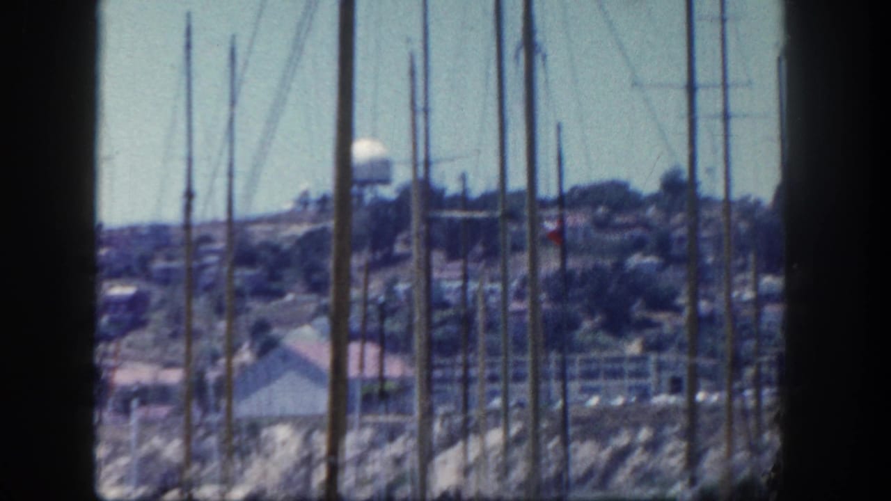 San Diego marina masts in the foreground with hillside homes and a water tower in the distance.