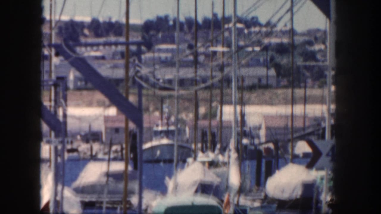 Marina view with sailboat masts, covered boats, water, and dark foreground framing.