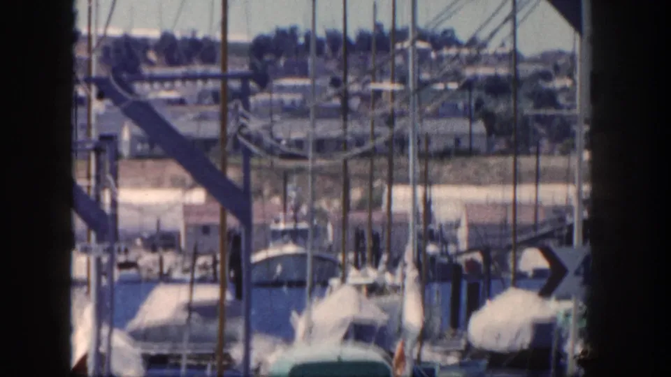 1962 San Diego marina footage showing docked boats, masts, water, and dark vertical foreground framing during a slow pan.