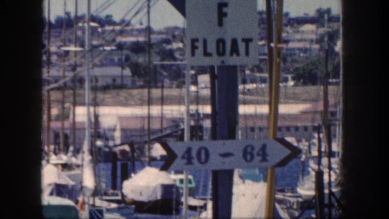 1962 San Diego marina frame with an F Float sign, slip 40-64 arrow, docked boats, and many sailboat masts.