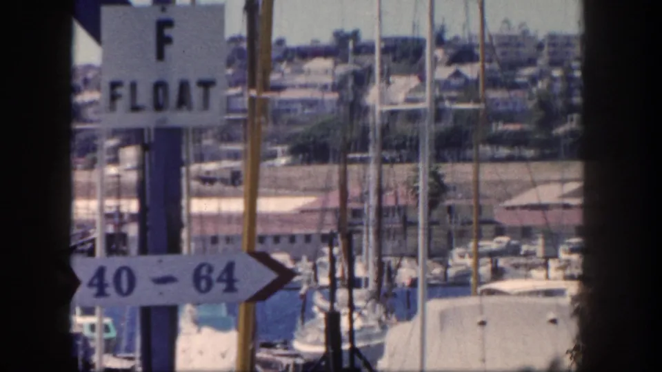 The pan passes closer to the F Float and 40-64 slip signage, with masts, dock structures, and boats behind it.