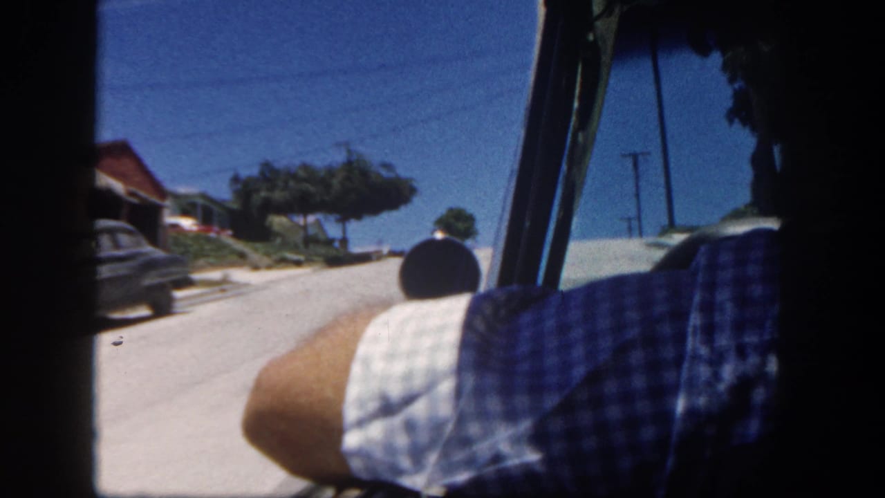 Passenger-side view from a moving car on a sunny residential street.