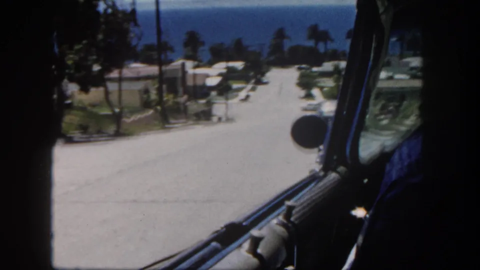 Interior 8mm car view of a steep San Diego hillside street with curbside homes, utility poles, palms, and ocean beyond.