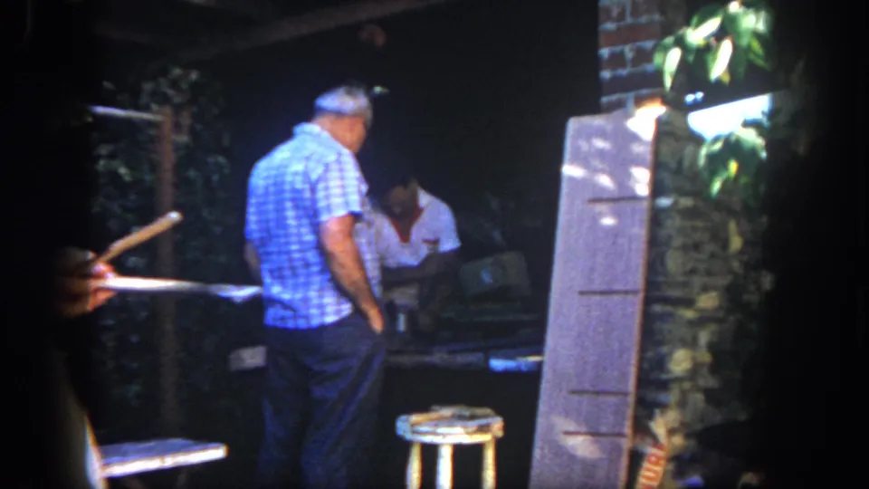 1962 San Diego workshop frame showing two adult men near a table, with an additional hand or object visible at the left edge of the film frame.