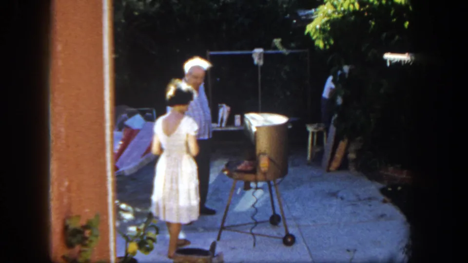 At the end of the clip, the woman stands with her back to the camera at the grill as the man looks on.