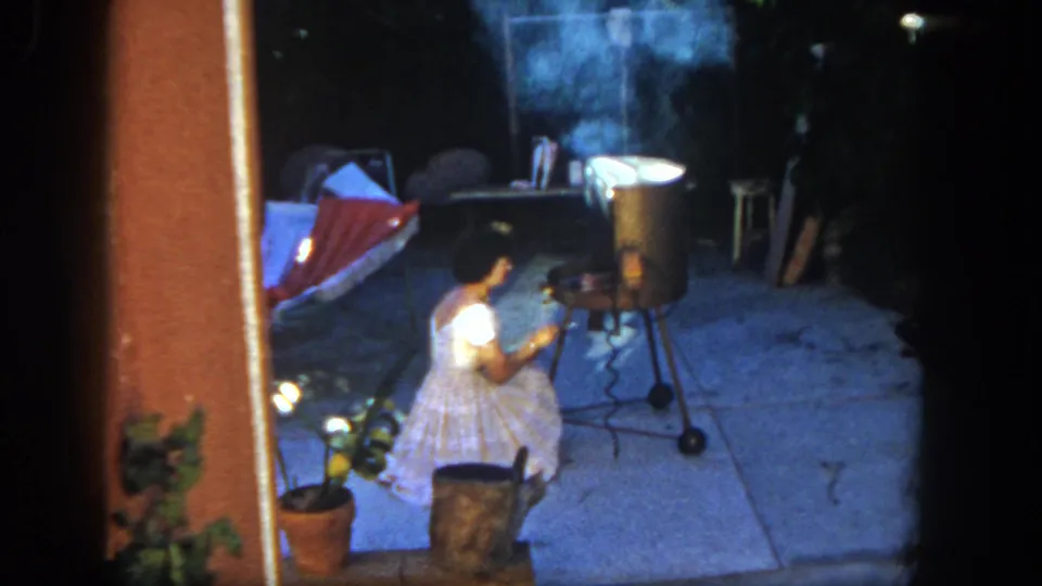 San Diego 1962 8mm footage shows a young girl seated near a smoking metal grill, with a hammock and patio objects behind her.