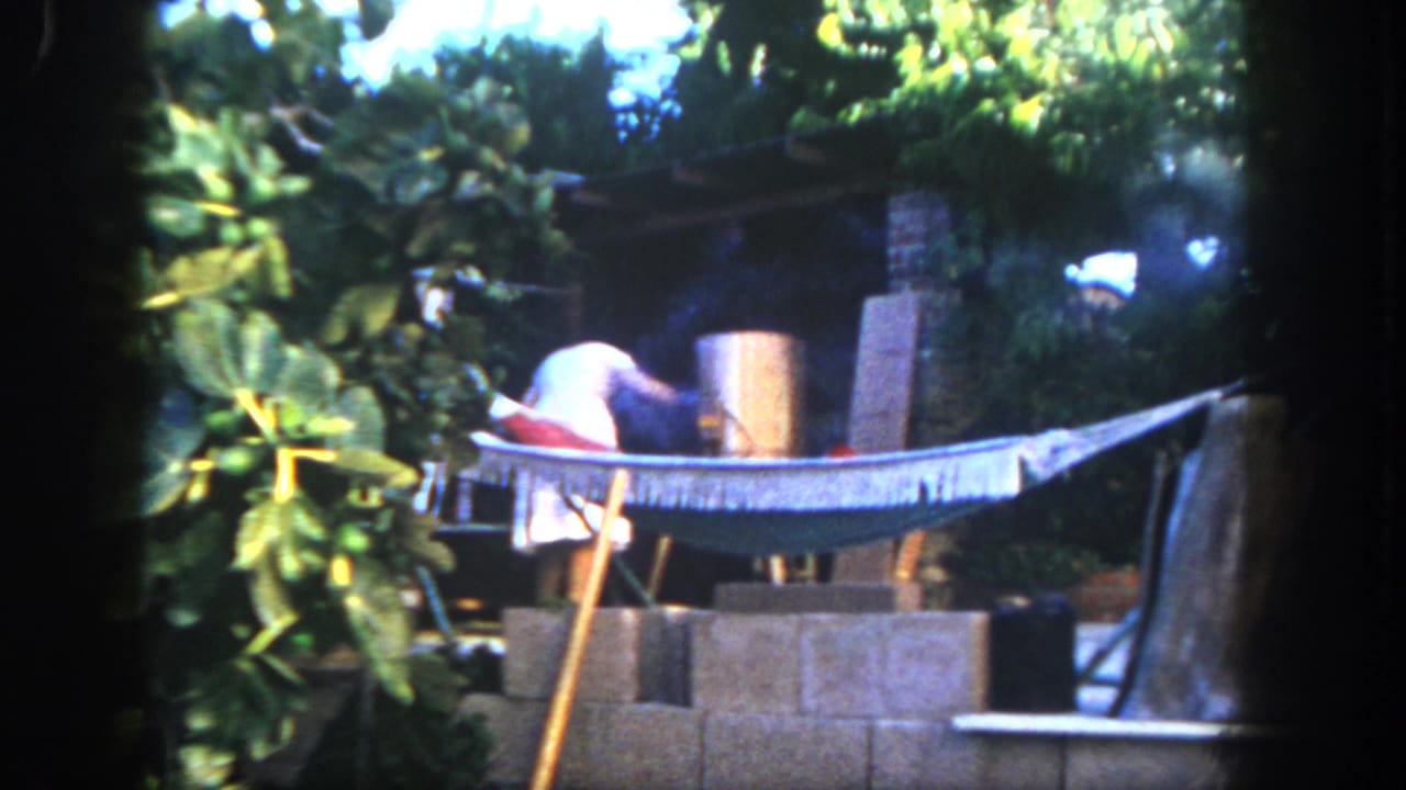 Person near a smoking cylindrical grill beside a hammock and cinder blocks.