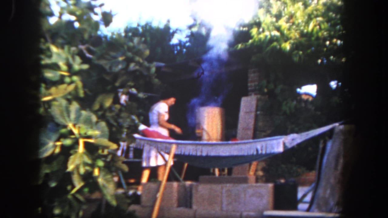 1962 San Diego frame with the woman working beside a smoking barrel in a lush garden, with a hammock stretched across the foreground.
