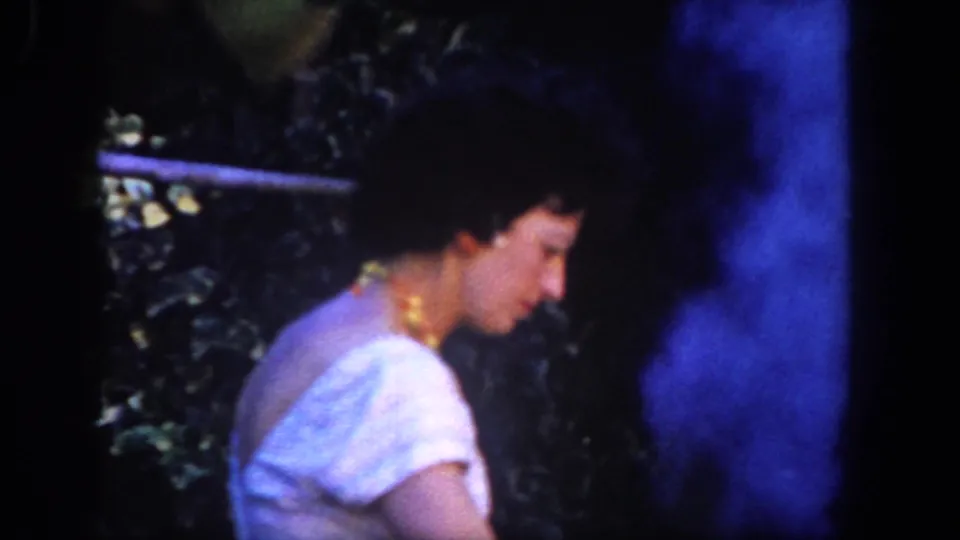 The 1962 San Diego footage shows the woman in profile near thick blue barbecue smoke, with foliage and fencing behind her.