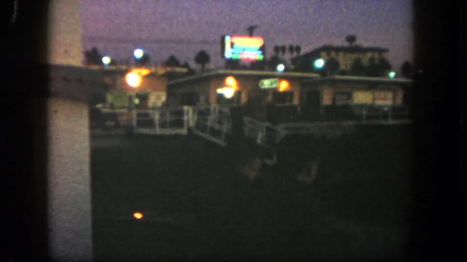 A distant nighttime view shows motel buildings, parked cars, exterior lights, and glowing signs in the 1962 San Diego home movie.