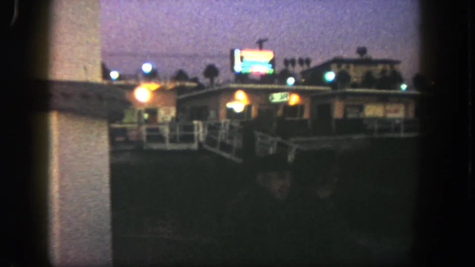 1962 San Diego home-movie frame showing a low building and glowing sign seen through dark foreground edges.