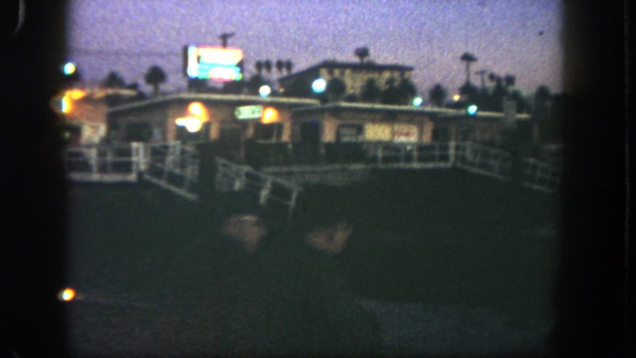 San Diego 1962 frame with a softly focused commercial building, illuminated signs, railing and dusky sky in 8mm texture.