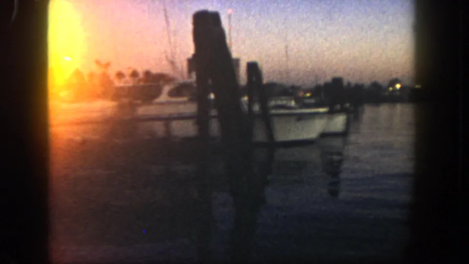 1962 San Diego home-movie frame showing dark dock pilings and water silhouetted by warm sunset glare.