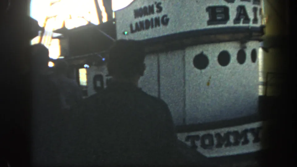 A silhouetted man stands close to the Tommy Boy boat at Horn's Landing in San Diego, with portholes and cabin signage visible.