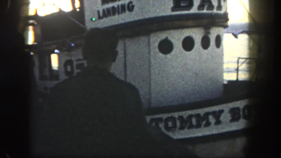 Final 1962 San Diego frame showing a man silhouetted in front of the moored Tommy Boy boat at dusk.