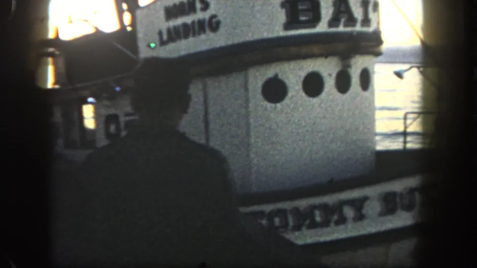 1962 San Diego 8mm frame showing a silhouetted person beside a bait boat with HORN'S LANDING lettering and sunlit water beyond.
