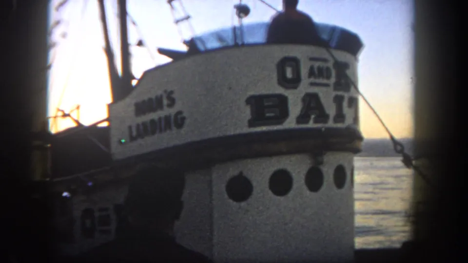 Final 1962 San Diego frame of the bait boat at golden hour, showing cabin signage, portholes, rigging, water, and silhouetted figures.