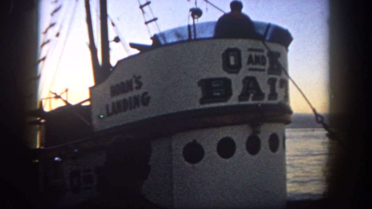 Fishing boat cabin with bold lettering, rigging, and silhouetted deck figures at sunset.