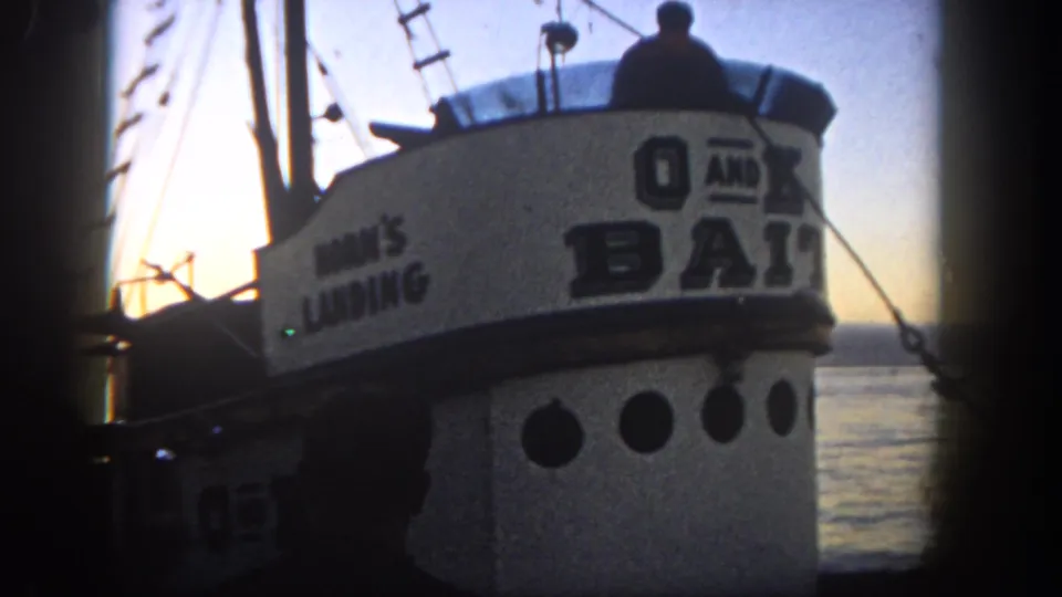 1962 San Diego harbor footage showing a fishing boat cabin with visible lettering, rigging, and dark figures against the evening light.