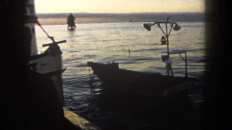 San Diego harbor view from 1962 showing a silhouetted small boat near dock equipment, with calm water and a distant boat in evening light.