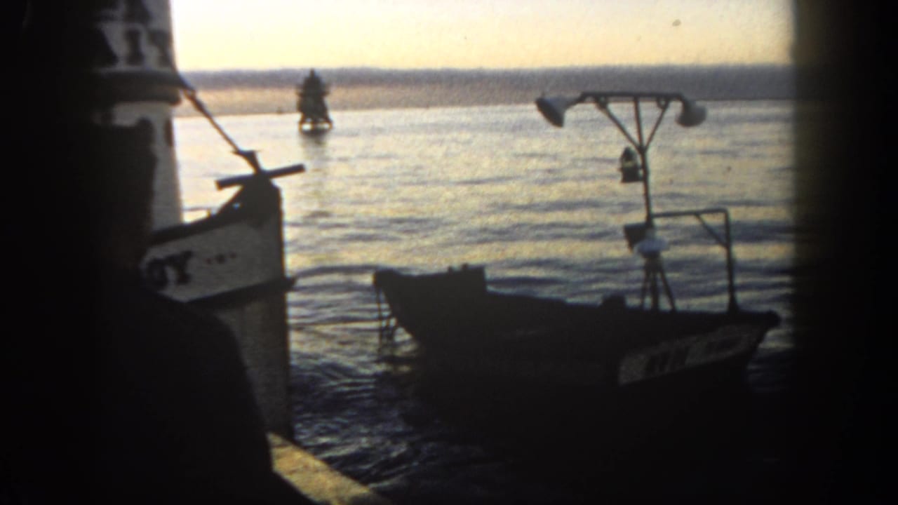 Silhouetted dockside view of a small boat floating on harbor water at dusk.