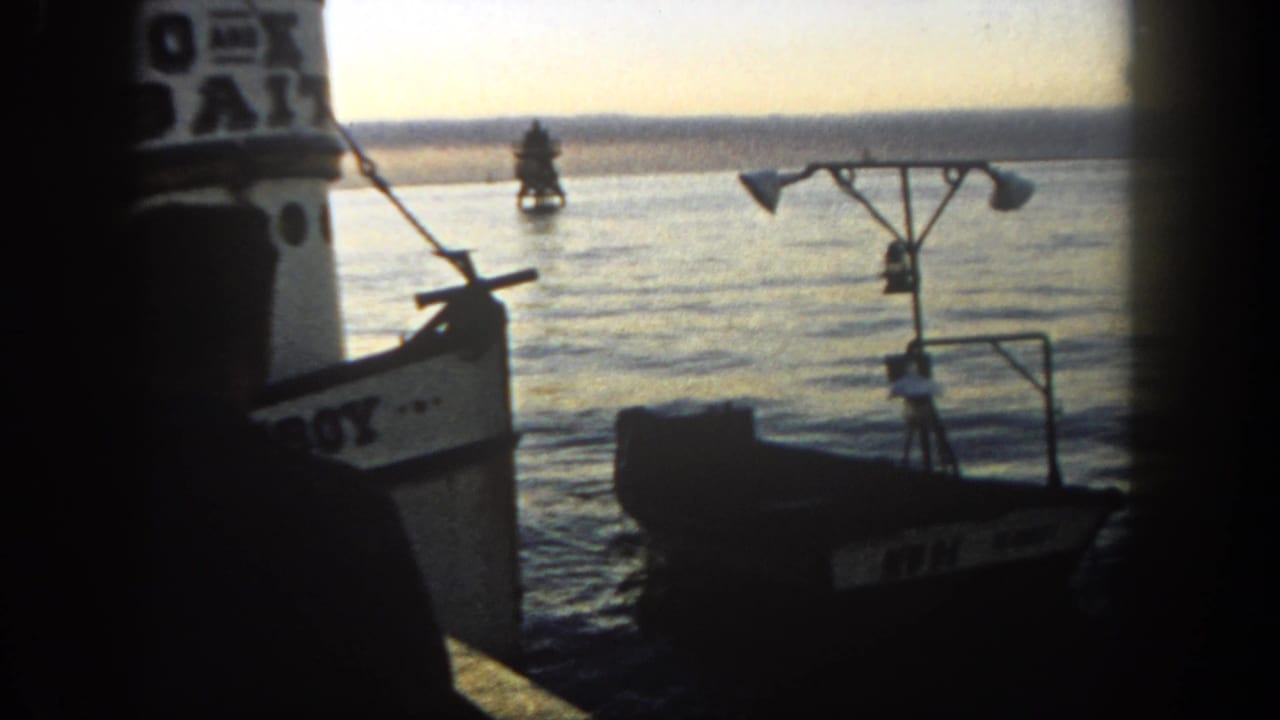 A small empty boat drifts beside a larger vessel in 1962 San Diego harbor, with a buoy visible across the water.