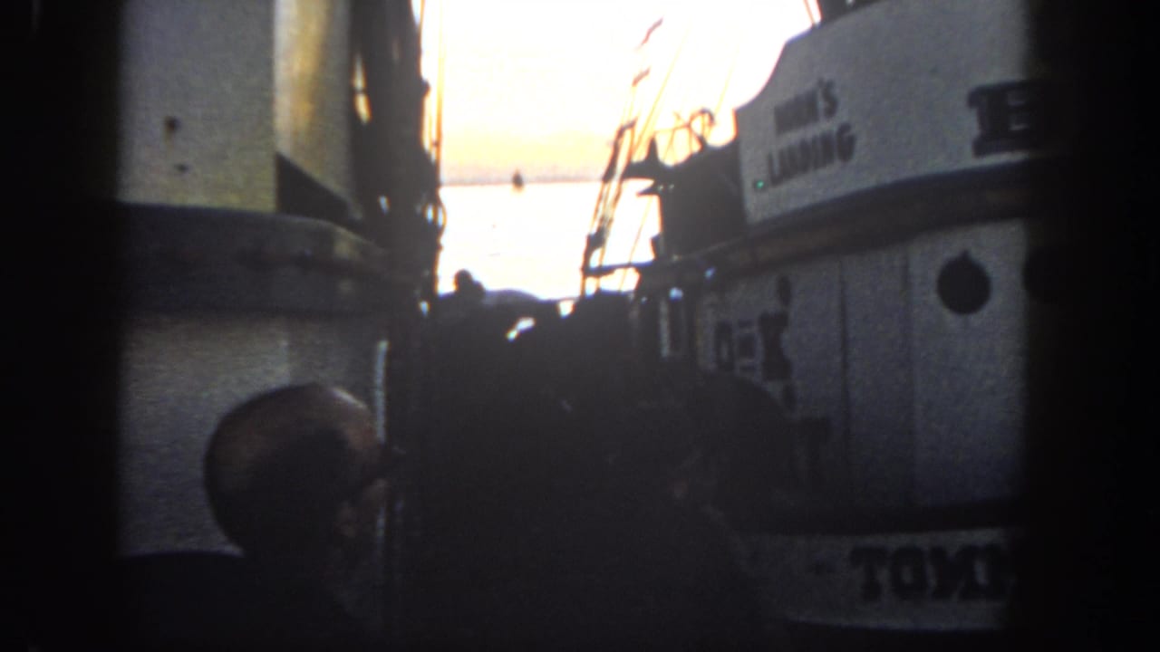San Diego harbor scene from 1962 with adjacent boats, silhouetted people, cabin windows, and bright sunset water beyond.