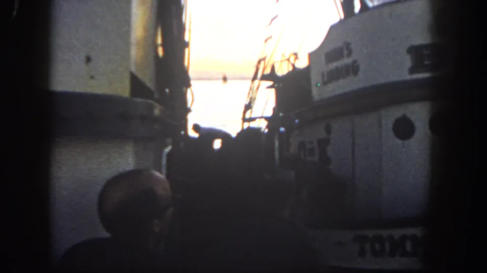 San Diego harbor home-movie frame from 1962 showing close boats, a foreground silhouette, rigging, and bright evening water.