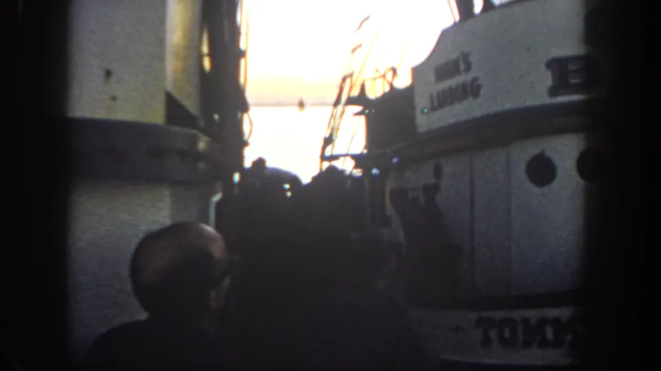 1962 San Diego-area 8mm frame showing silhouetted figures on a fishing boat deck beside a cabin, with sunset over the ocean.