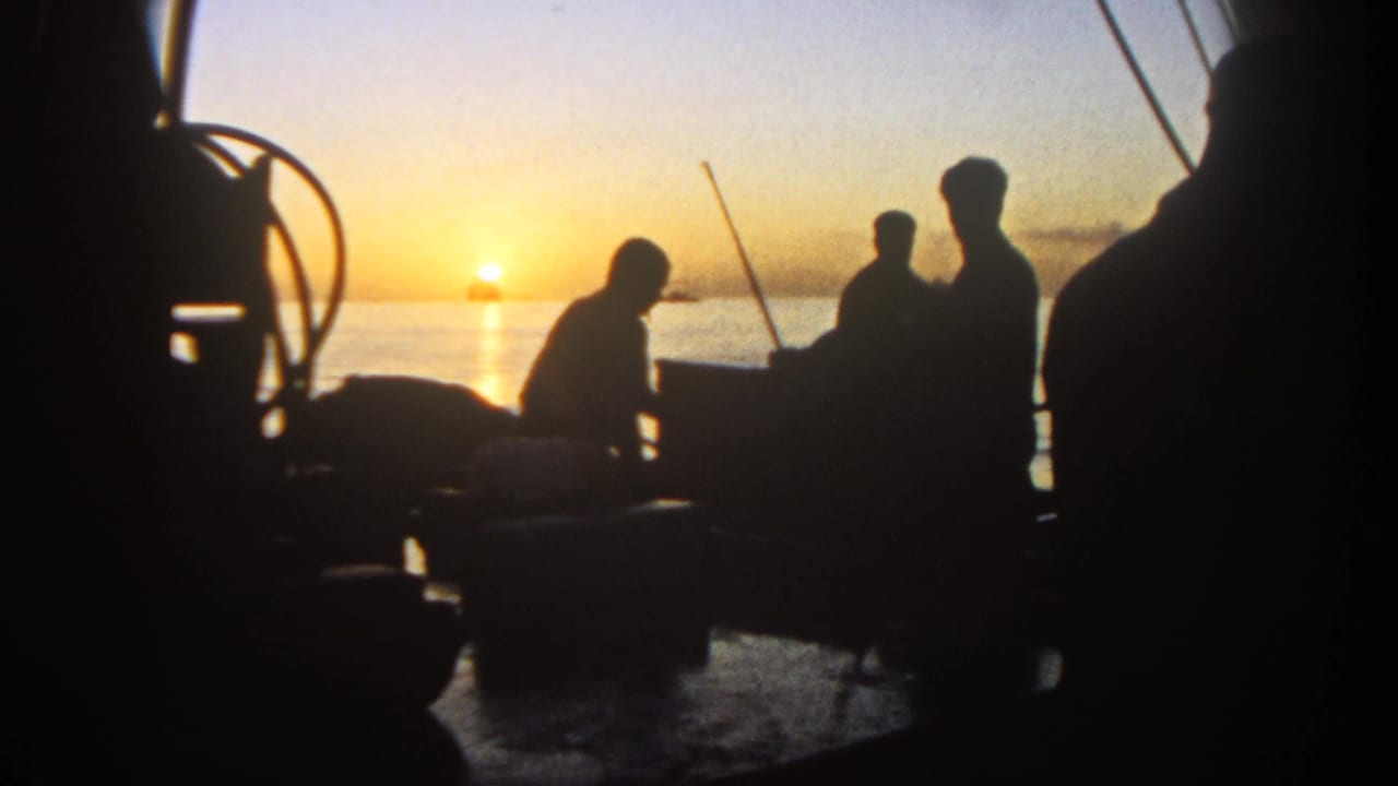 Dark silhouettes on a boat deck with fishing rods against a sunset horizon.