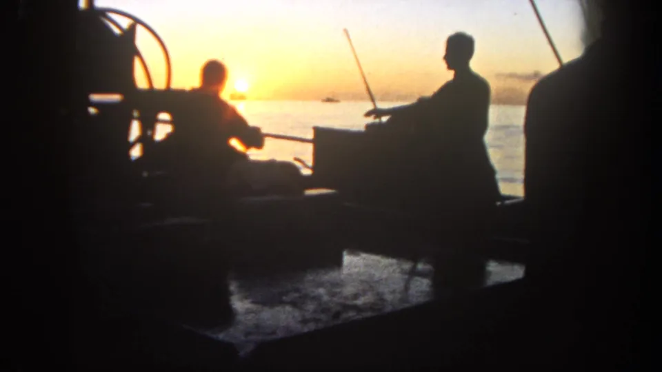 Backlit 8mm frame from 1962 showing people on a San Diego fishing boat deck, with rods, railing, and sunset glare across the ocean.