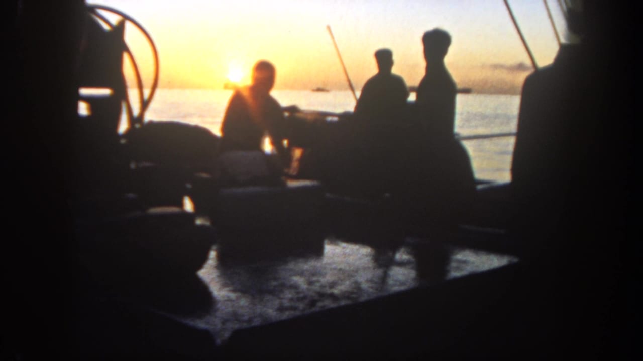 Several silhouetted figures gather on a boat with fishing rods near a low sun.