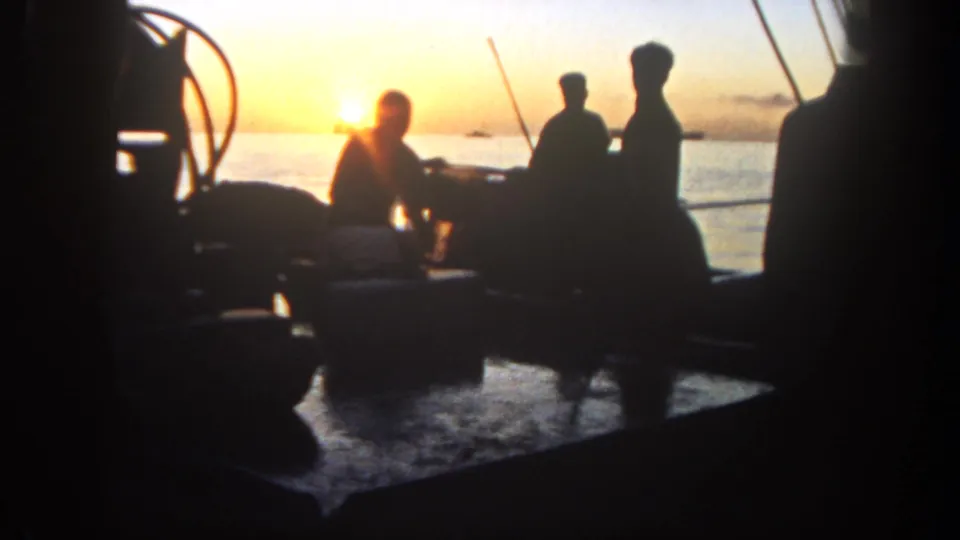 Silhouetted men on a fishing boat in 1962 San Diego appear to talk and handle rods against a bright sunset over the ocean.