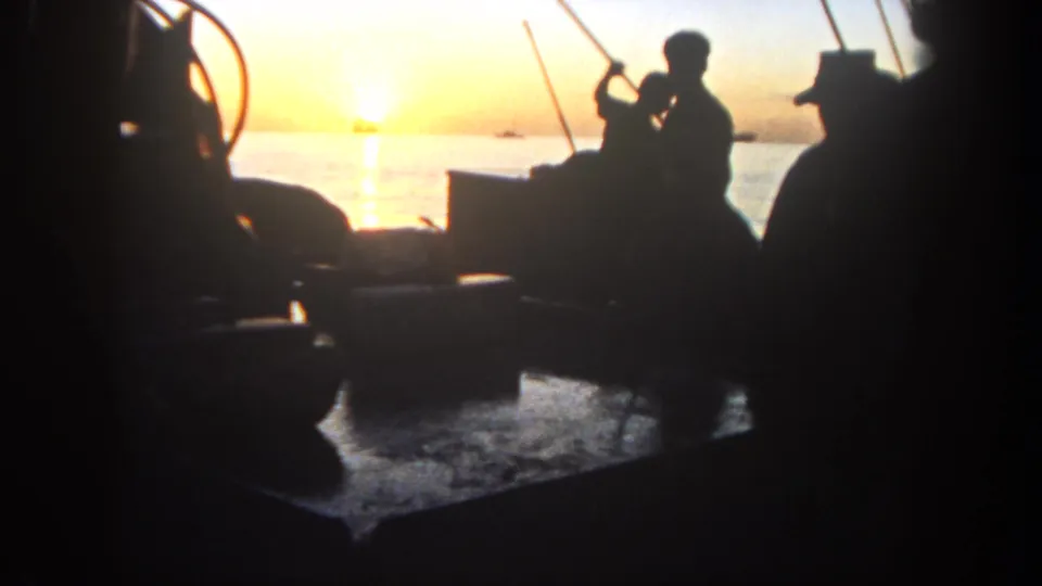 On a small boat off San Diego in 1962, a silhouetted fisherman holds a rod while another seated figure faces the bright sunset water.