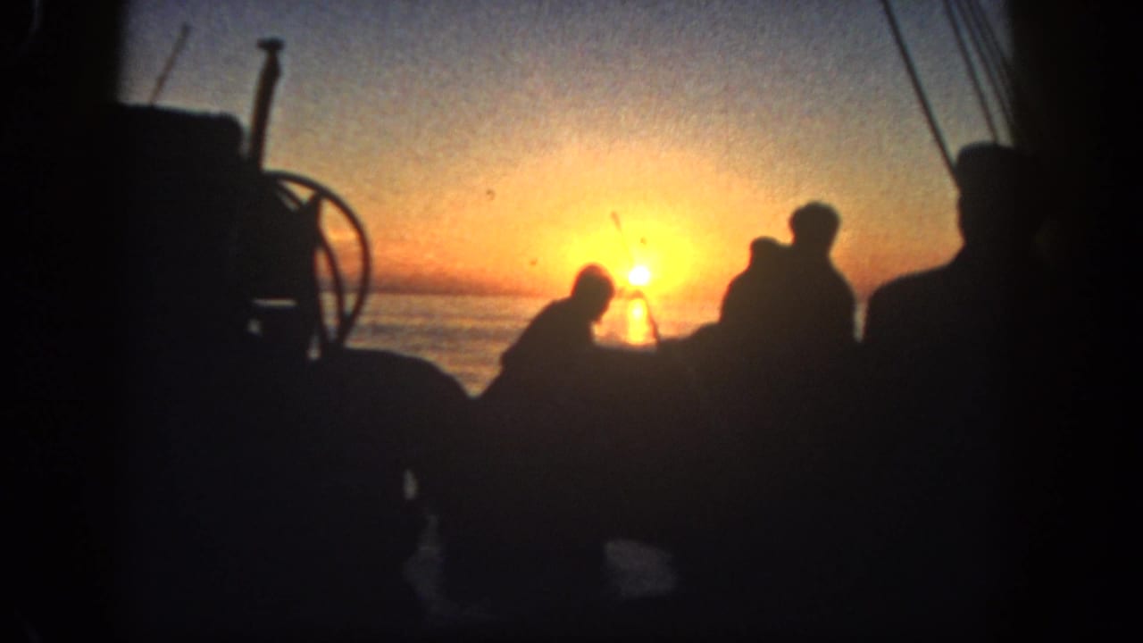 Silhouetted people on a boat at sunrise with water and rigging behind them.
