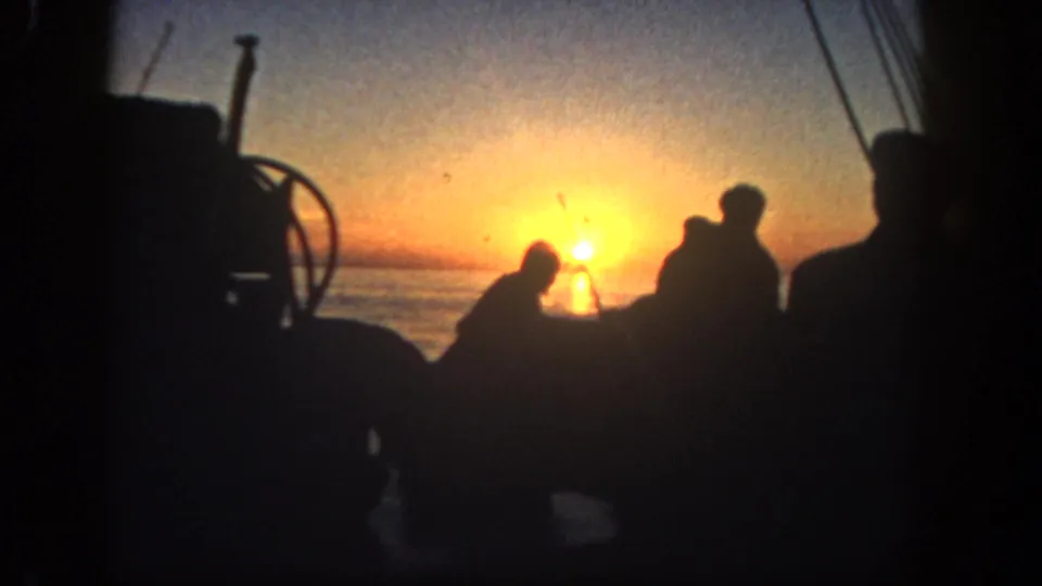 1962 San Diego 8mm frame showing silhouetted figures on a boat deck against orange sunrise over water.