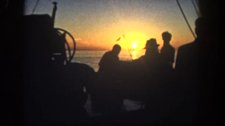 1962 San Diego 8mm frame with several silhouetted figures, rigging, and boat structure against a bright coastal sunrise.