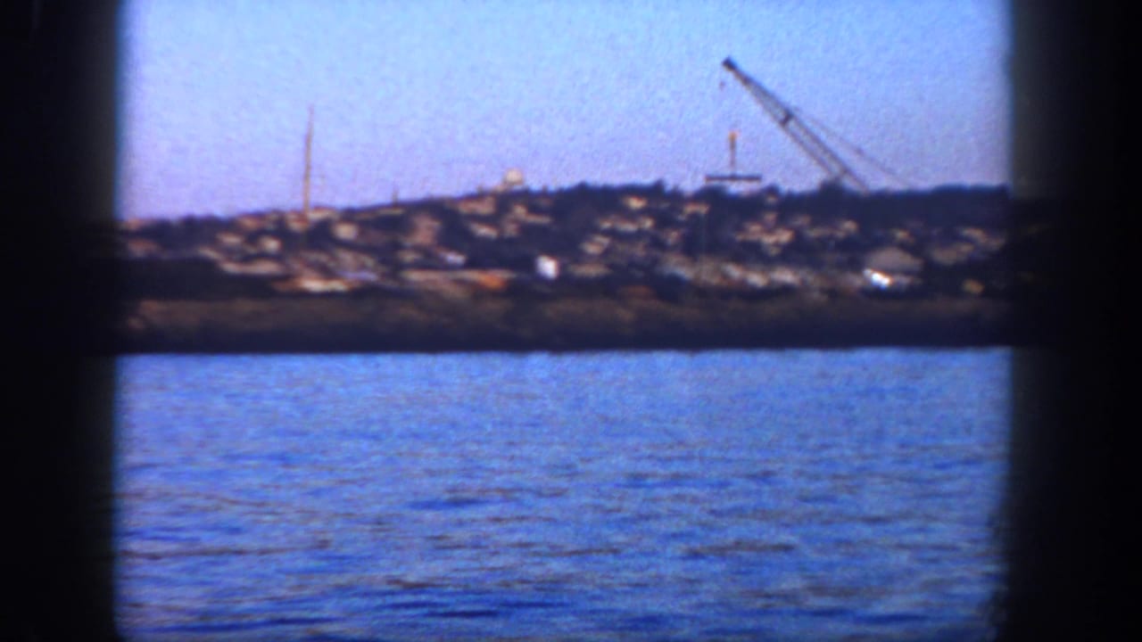 Distant harbor shoreline with water in the foreground and a crane on the horizon.