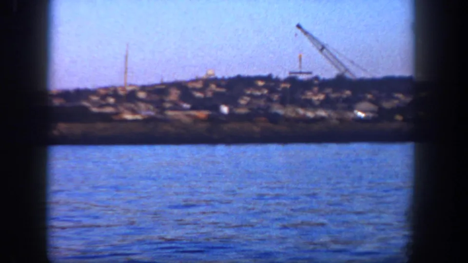1962 San Diego harbor view with blue water, a distant shoreline, and a crane visible near the horizon.