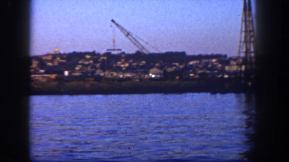 1962 San Diego 8mm harbor frame showing shoreline structures, a crane, and a tall tower across the water.