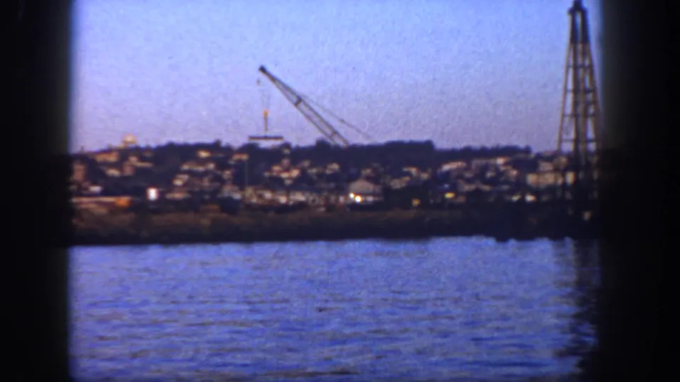 1962 San Diego harbor view from a boat, with blue water, a distant crane, and a tall tower near the frame edge.