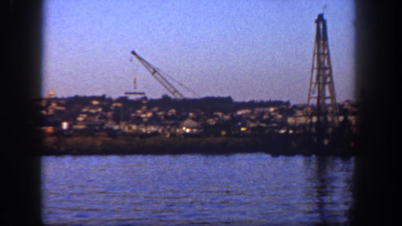 1962 San Diego shoreline seen from across the water, with a crane and tall tower near hillside housing.