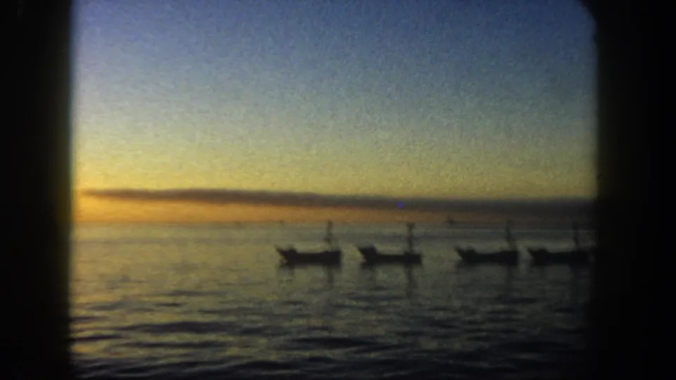 1962 San Diego waterfront sunset with several anchored boats silhouetted against calm sea and distant horizon.