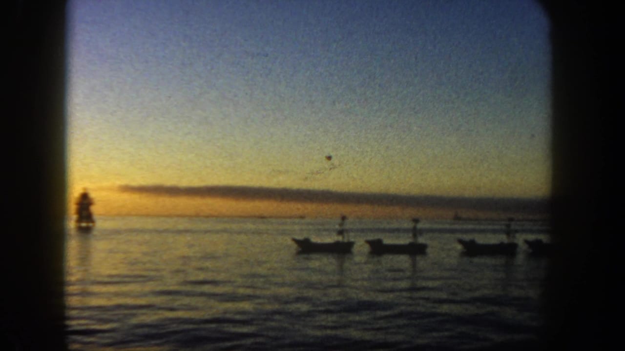Sunset over calm ocean with silhouetted boats and a distant navigation marker.