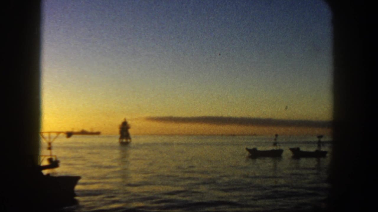 1962 San Diego coastal view through a dark boat opening, with silhouetted small craft, a distant marker, and warm sunset light on the water.