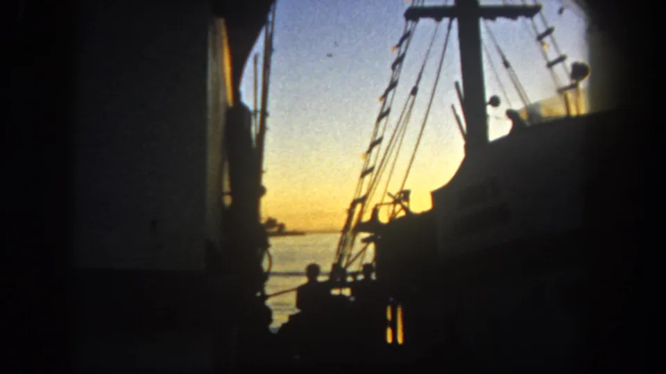The 8mm frame shows San Diego harbor rigging, a dark deck figure, calm water, and warm sunset color in 1962.