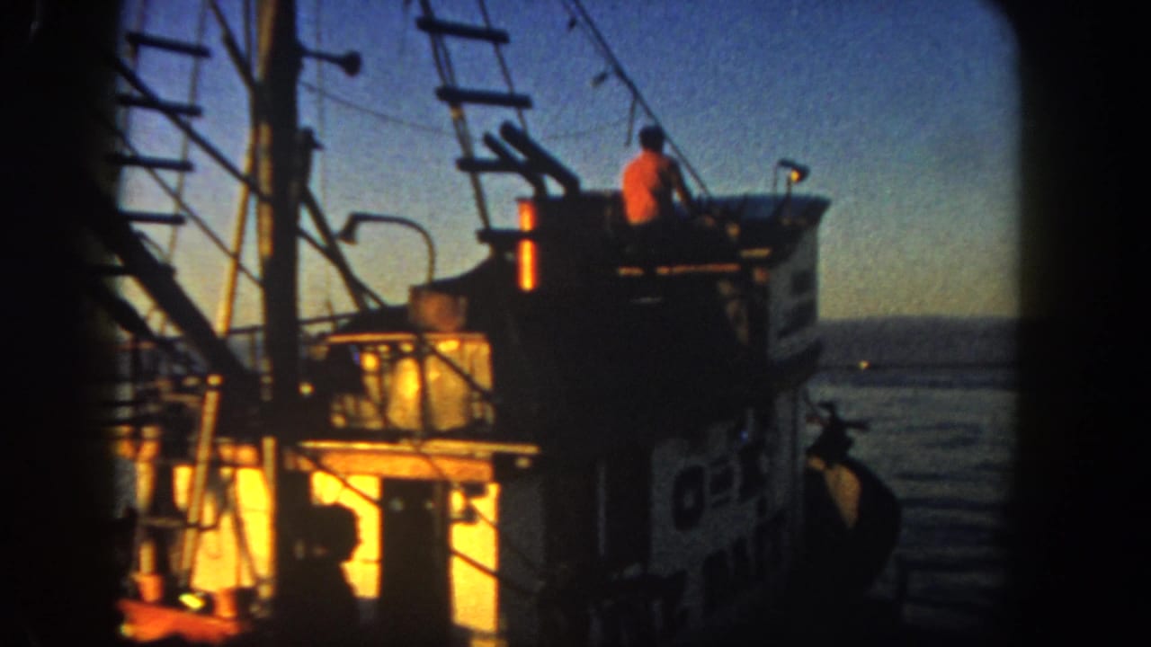 Fishing boat cabin and rigging at dusk with a crew member silhouetted near the upper deck.