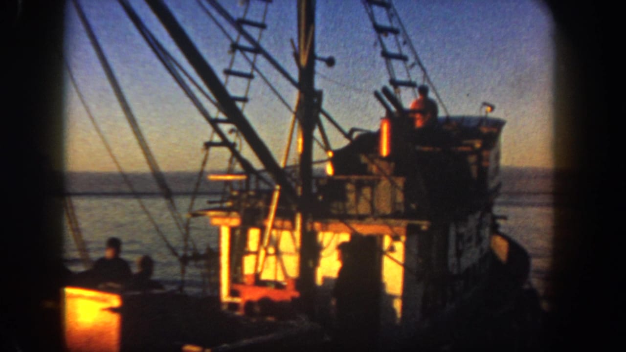 Fishing boat rigging and cabin lit by sunset with crew silhouettes on deck.