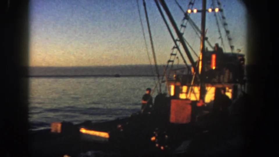 The final 1962 San Diego frame shows a fishing boat from the side or stern area, with rigging, warm cabin light, a crew figure near the rail, calm water, and a fading horizon.